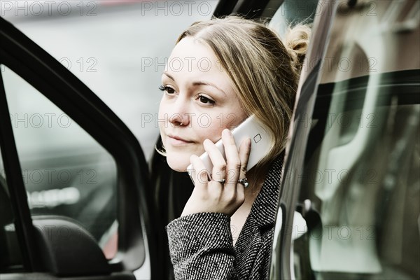 Young woman sits at an open door with her smartphone in the car