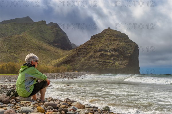 Tourist sits on the beach of Parque Ruben Perez in front of Charco de la Aldea