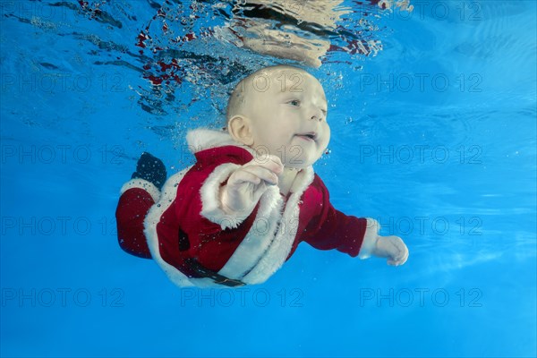 A little boy in Santa's cost swims underwater in the pool