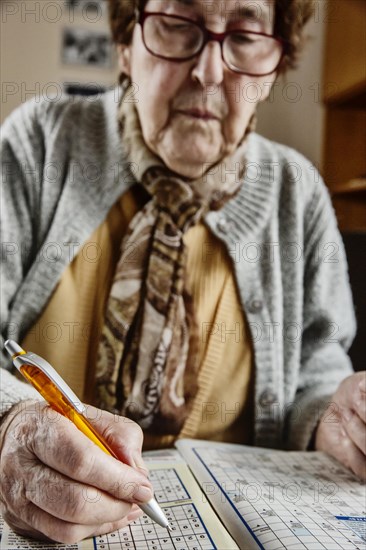 Senior sits at the table at home and solves puzzles