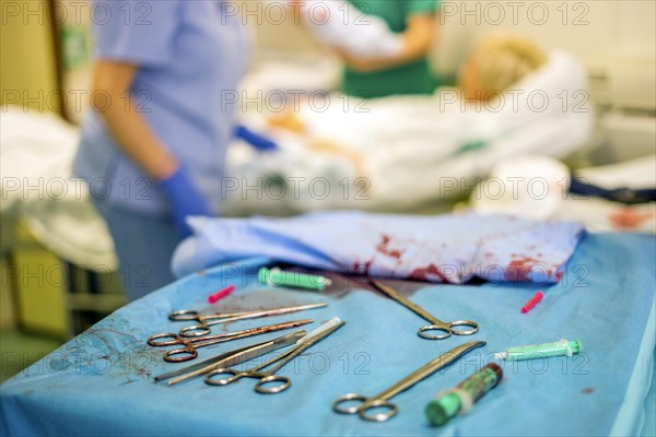 Silver gynecologist tools used during childbirth and mother and hospital staff in the background