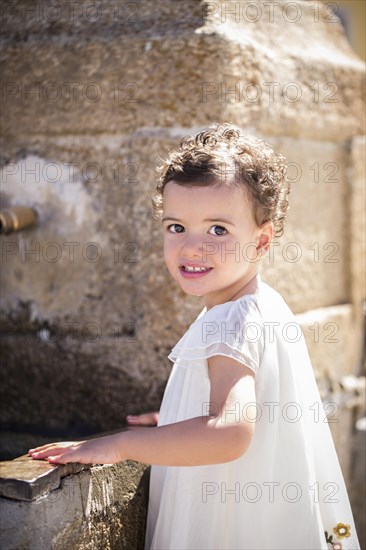 Little girl in white dress stands by a fountain
