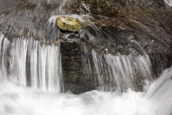 Stone lies in front of a small waterfall in current