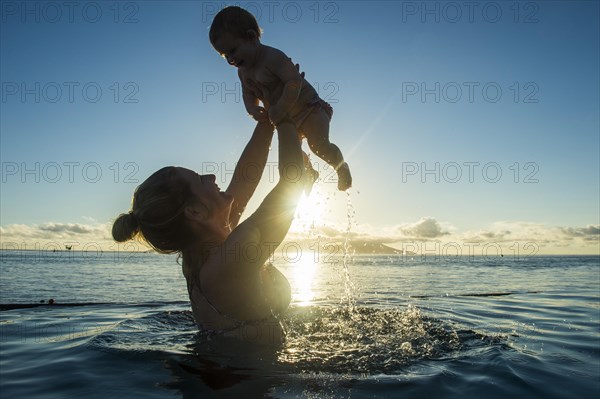 Mother playing with her little baby in the water at sunset