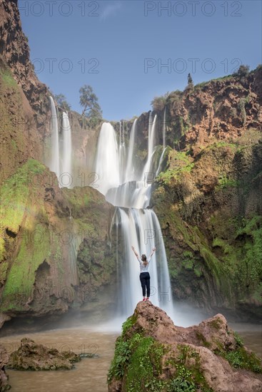 Young woman standing on a stone in front of Ouzoud waterfalls and cascades