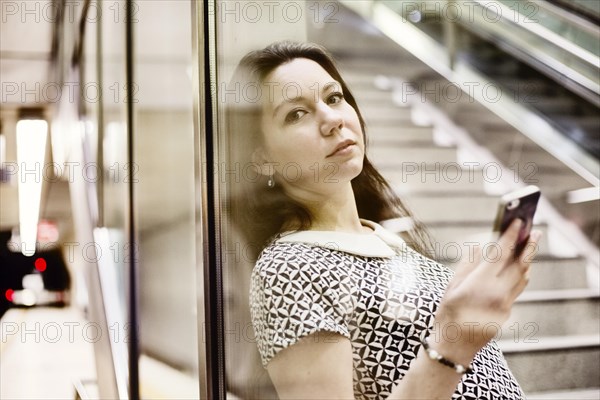 Young woman posing with smartphone behind a glass wall in a subway station