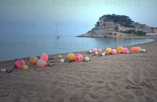 Orange and pink buoys on the sandy beach of Tossa de Mar