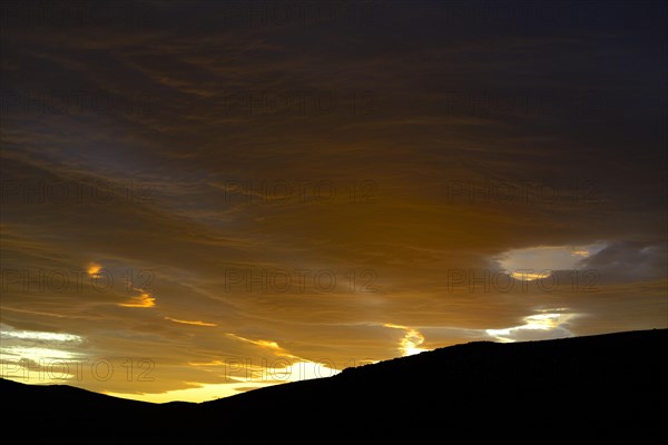 Dramatic sunset with rising storm clouds in front of mountain silhouette