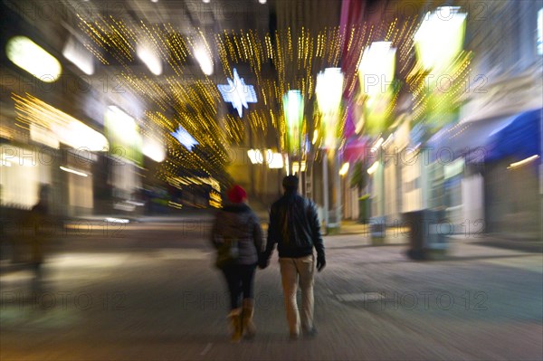 Couple goes hand in hand through a Christmas illuminated street