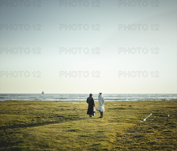 Two women standing at the coast looking at the horizon