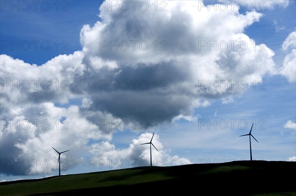 Silhouettes of wind turbines on a hill with cloudy sky