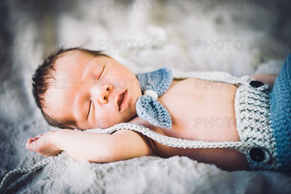 A newborn baby boy sleeping in blue and grey knitted bow tie and trousers