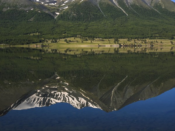 Khoton Lake with green forest landscape and water reflection of snow-covered mountains