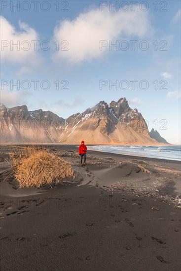 Man in red jacket walking on the black lava beach