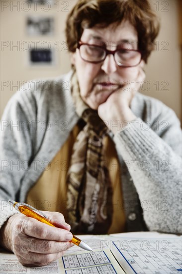 Senior sits at the table at home and solves puzzles