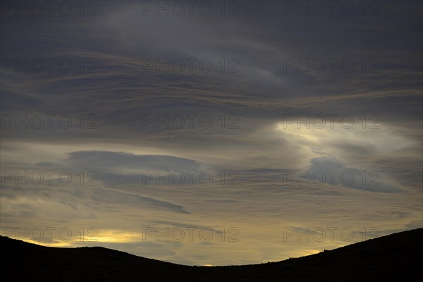 Dramatic sunset with rising storm clouds in front of mountain silhouette