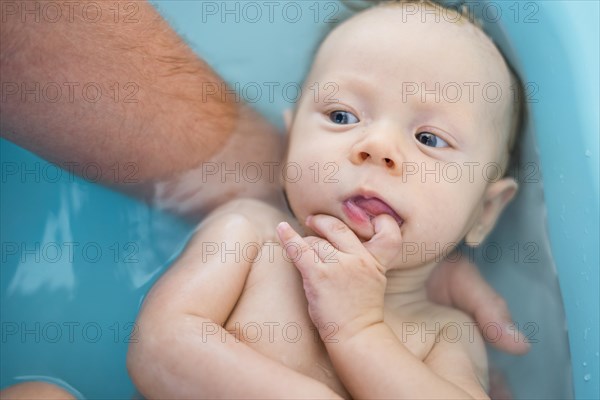 Baby boy thinking with his finger in a mouth while having a bath