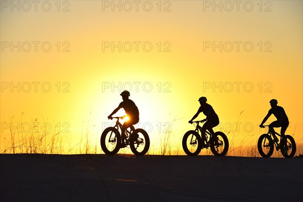 Three cyclists on fatbikes backlit at sunset