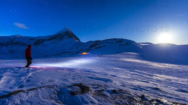 Person with tent on full moon in the snow