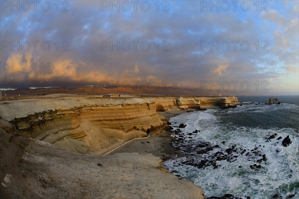 Rocky coast with arch La Portada at sunset with clouds