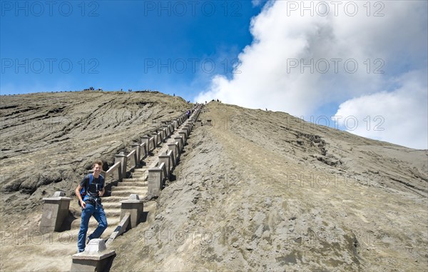 Young man on the stairs to the crater rim of the smoking volcano Gunung Bromo