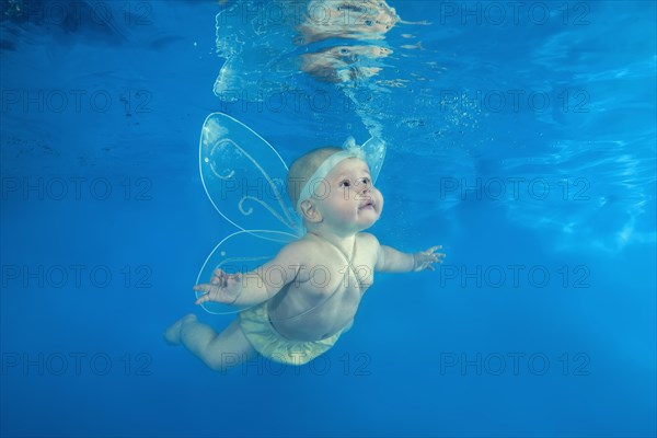 A little girl in a fairy costume swims underwater in the pool