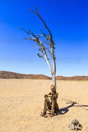 Cairn Lonely Man sits under a dried-up tree in Hartmann Valley