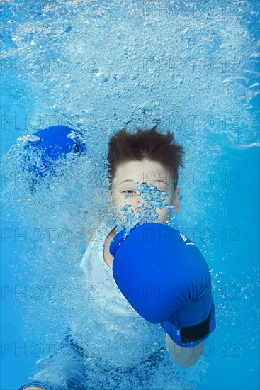 A boy in boxing gloves posing underwater in the pool