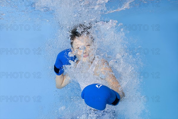 A boy in boxing gloves posing underwater in the pool