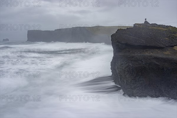 Couple stands above the Cliffs of Dyrholey at Storm