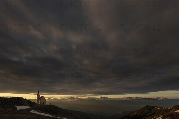 Latzfonser cross chapel at sunrise with dramatic clouds and South Tyrolean mountains