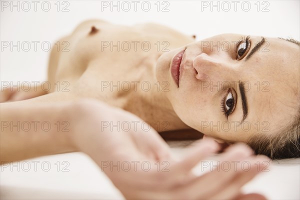 Young woman lying naked on a white background