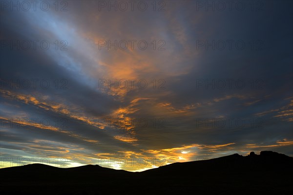 Dramatic sunset with rising storm clouds in front of mountain silhouette