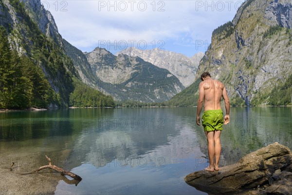 Young man in swimming trunks stands on a stone in Lake Obersee