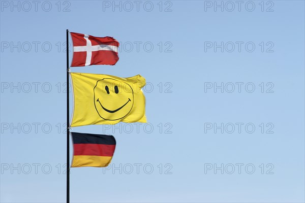 German and Danish flags waving together with a smiley flag on a flagpole
