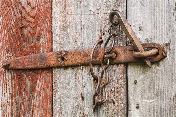 Close-up of rusted steel latch on old wooden grey and red painted barn door