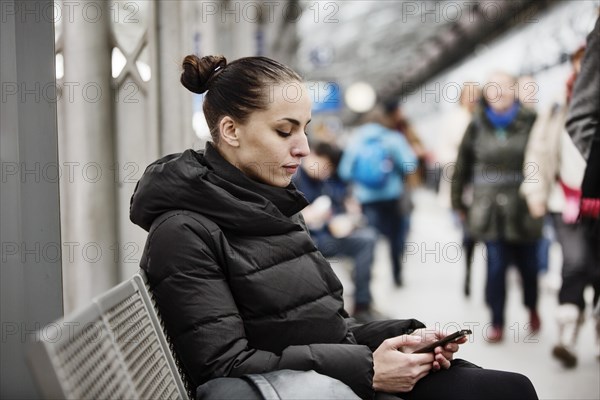 Young woman on a platform in the main station looks at her smartphone