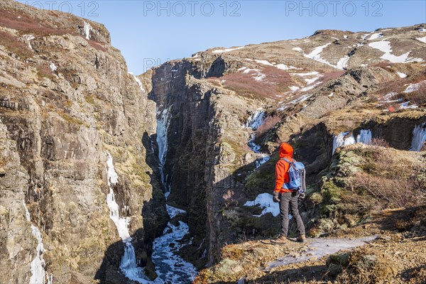 Man in orange jacket standing at the canyon of Glymur Waterfall