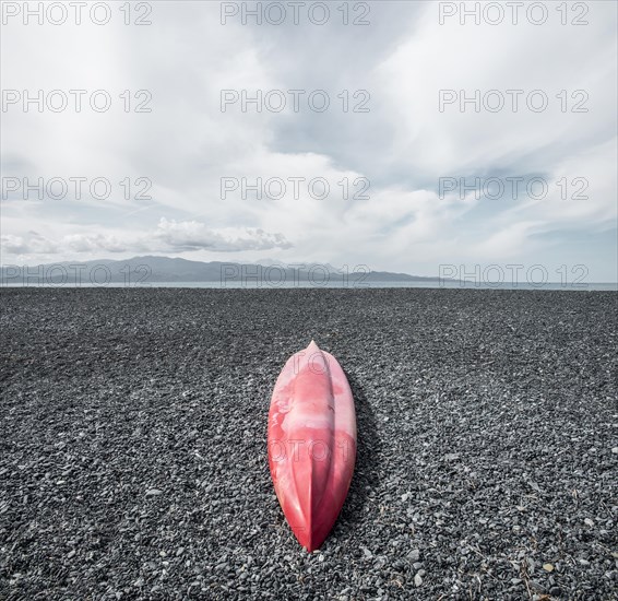 Red inverted canoe on the black stone beach of Albo