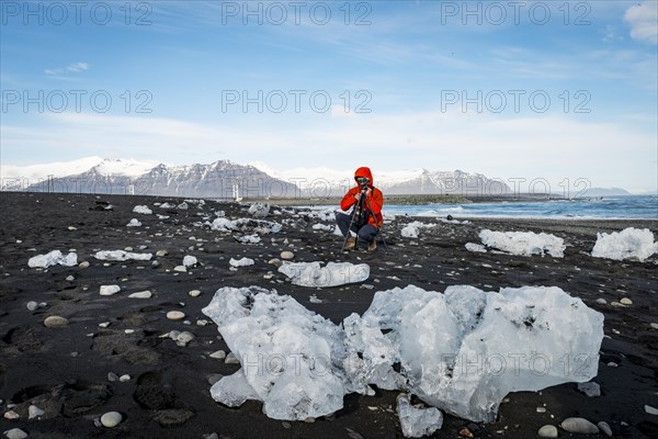 Tourist takes photos of ice floes on black lava beach