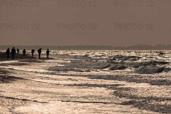 People on the beach by rough sea in the evening light