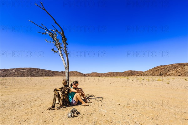 Young woman sitting under a dried tree next to a cairn Lonely Man