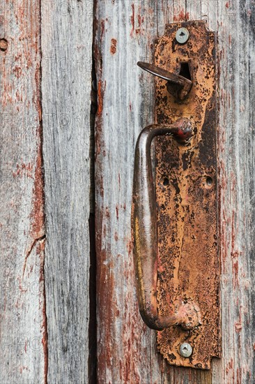 Close-up of rusted metal handle on old wooden grey and red painted barn door