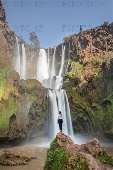 Young woman standing on a stone in front of Ouzoud waterfalls and cascades