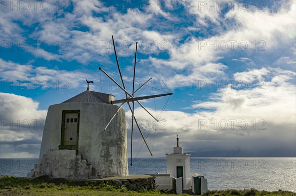 White windmill at the sea in front of a cloudy sky