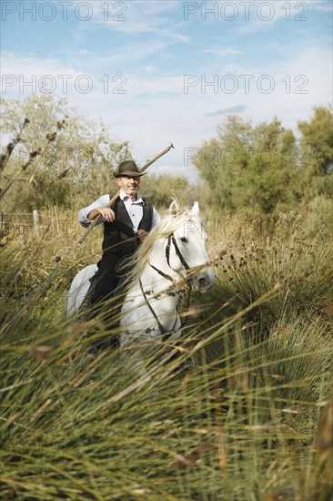 Gardian or traditional bull herder in typical working clothes galloping on a Camargue horse