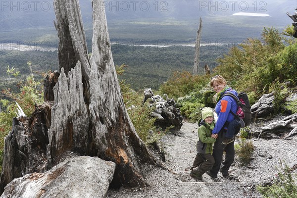 Woman with child hiking on crater of volcano Chaiten and volcanic eruption destroyed forest