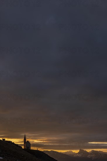 Latzfonser cross chapel at sunrise with dramatic clouds and South Tyrolean mountains