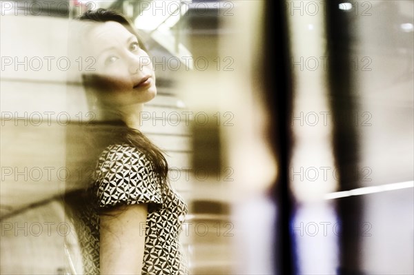 Young woman posing behind a glass wall in an underground station