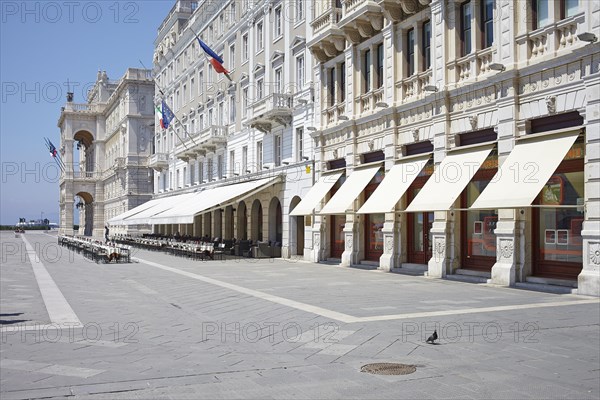 House facade with awnings and empty rows of chairs in front of a cafe on Piazza Unita d' Italia